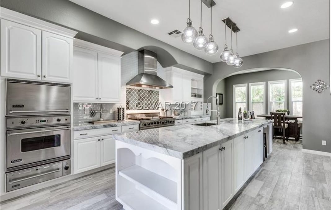 Modern white kitchen with island, gray walls, stainless steel appliances, and pendant lights.