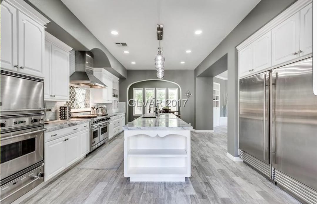 Modern kitchen with white cabinets, stainless steel appliances, marble island, and gray walls.