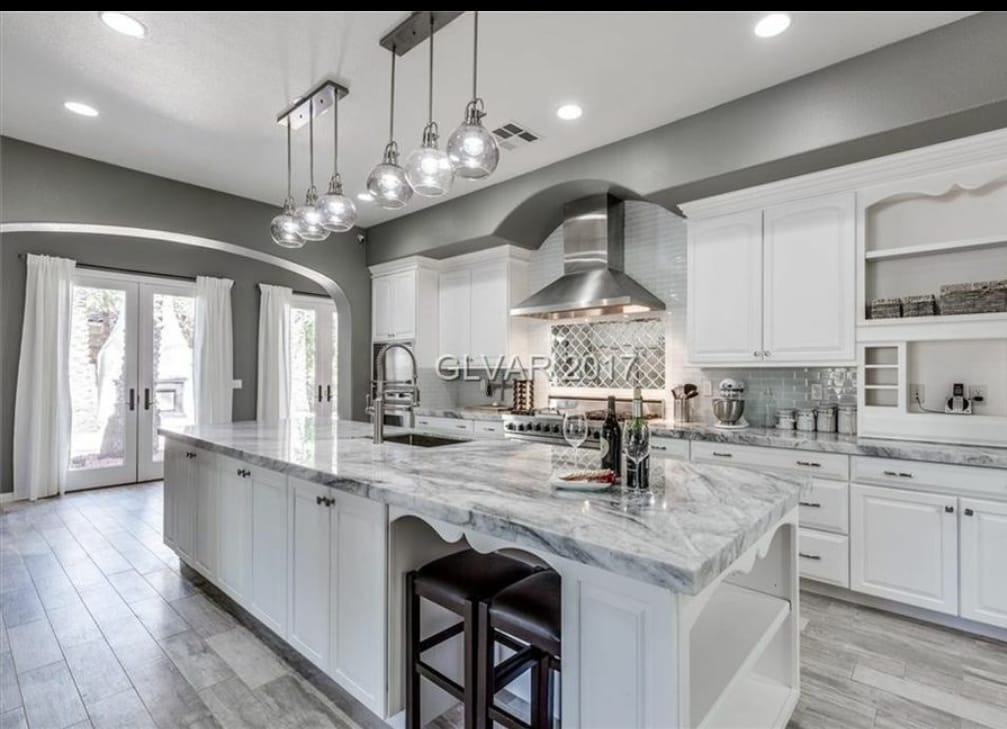White kitchen with large island, marble countertop, pendant lights, and stainless steel appliances.