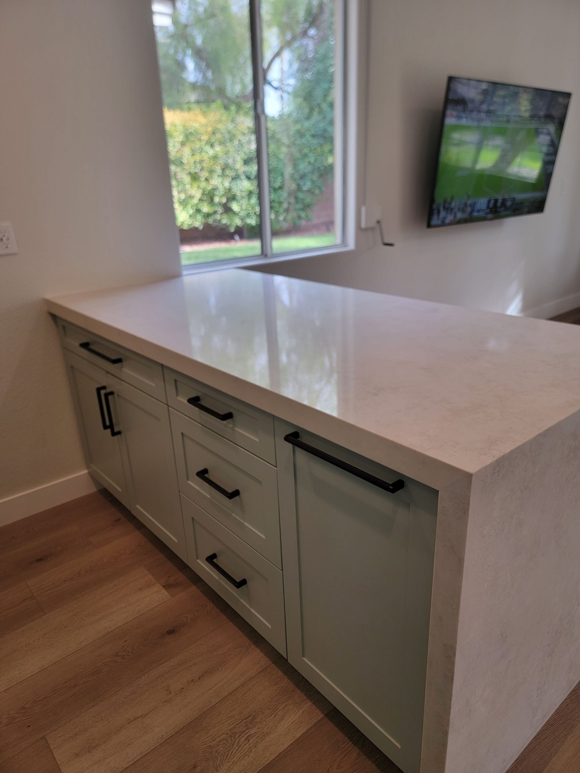 Light green kitchen island with a white countertop and black hardware, set in front of a window.