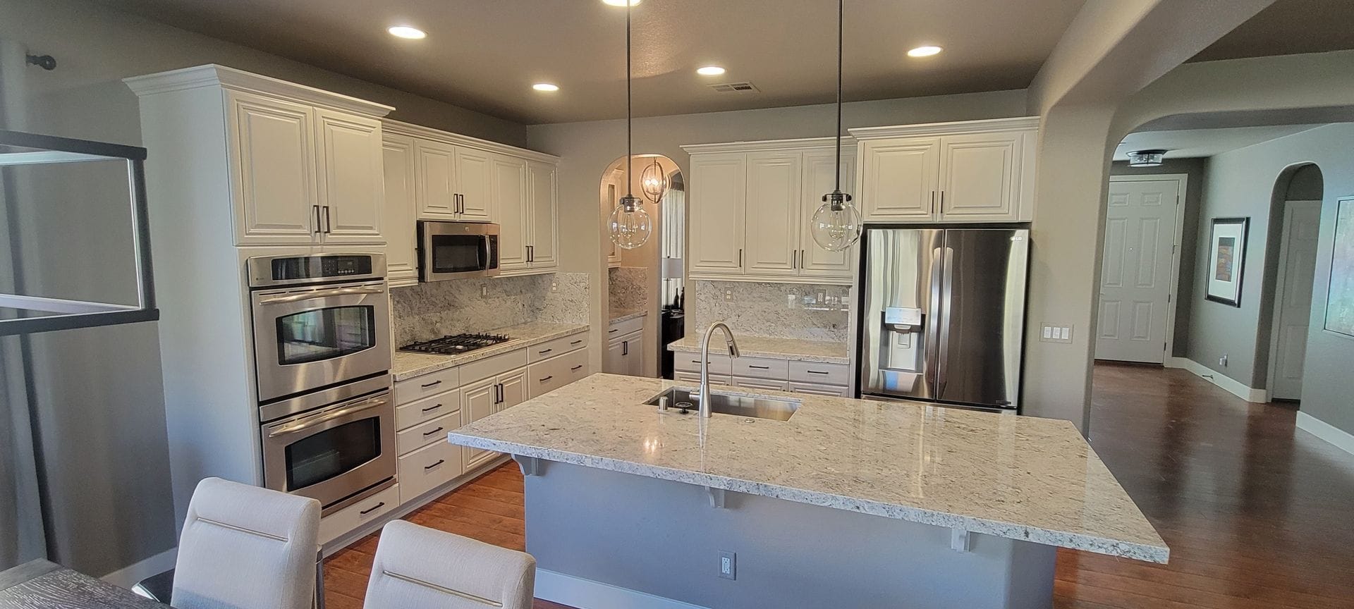 A modern white kitchen with stainless steel appliances, a large island, and wood floors.