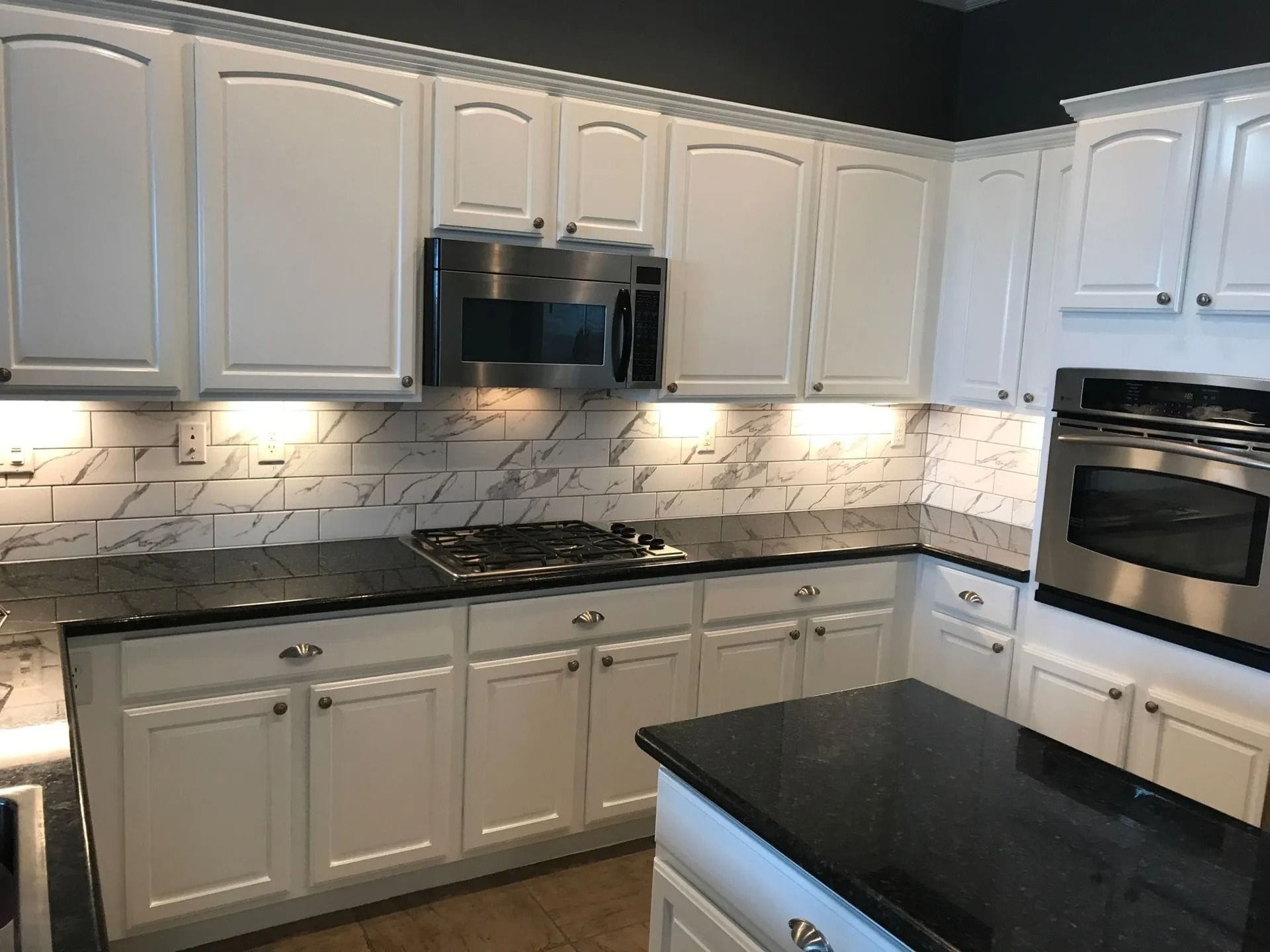 White kitchen cabinets with black countertops and stainless steel appliances.