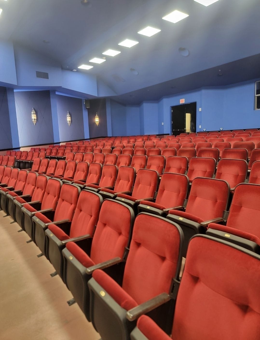 Rows of red theater seats in a blue-walled auditorium, rows leading to a stage.